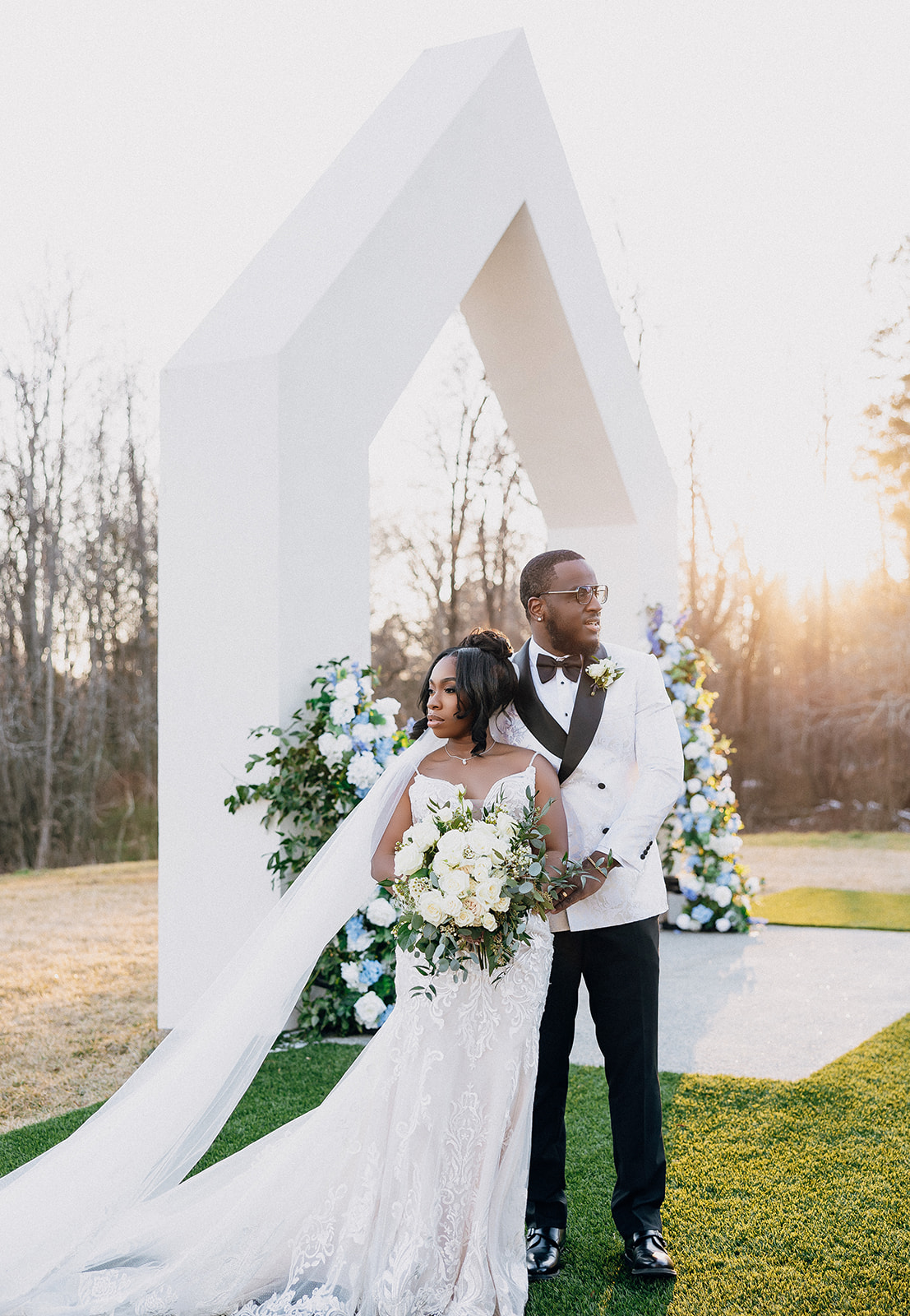 A couple poses for outdoor wedding portraits in front of a modern wedding arch.
