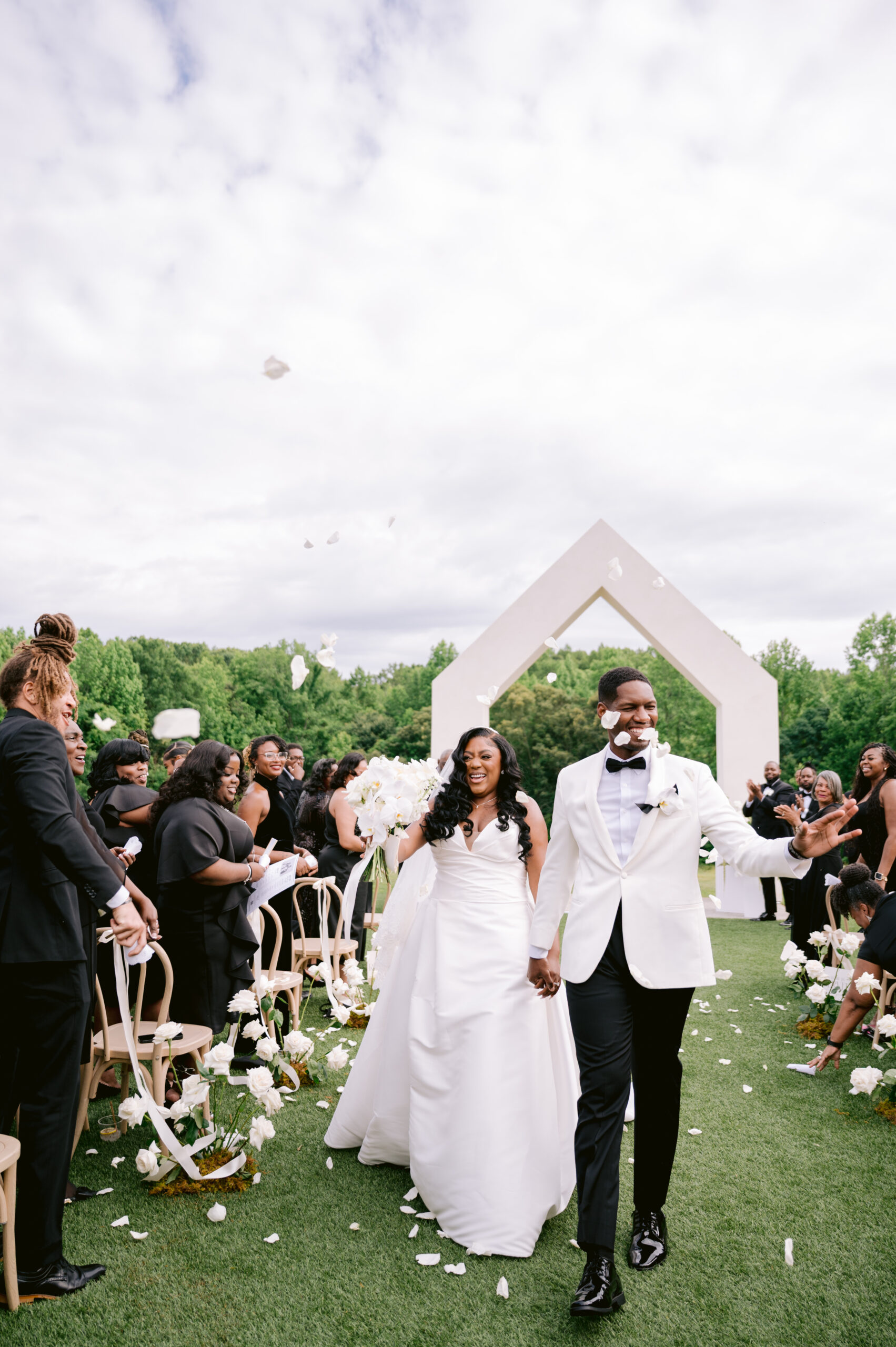 A bride and groom walking back down the aisle with white flower petals flying.