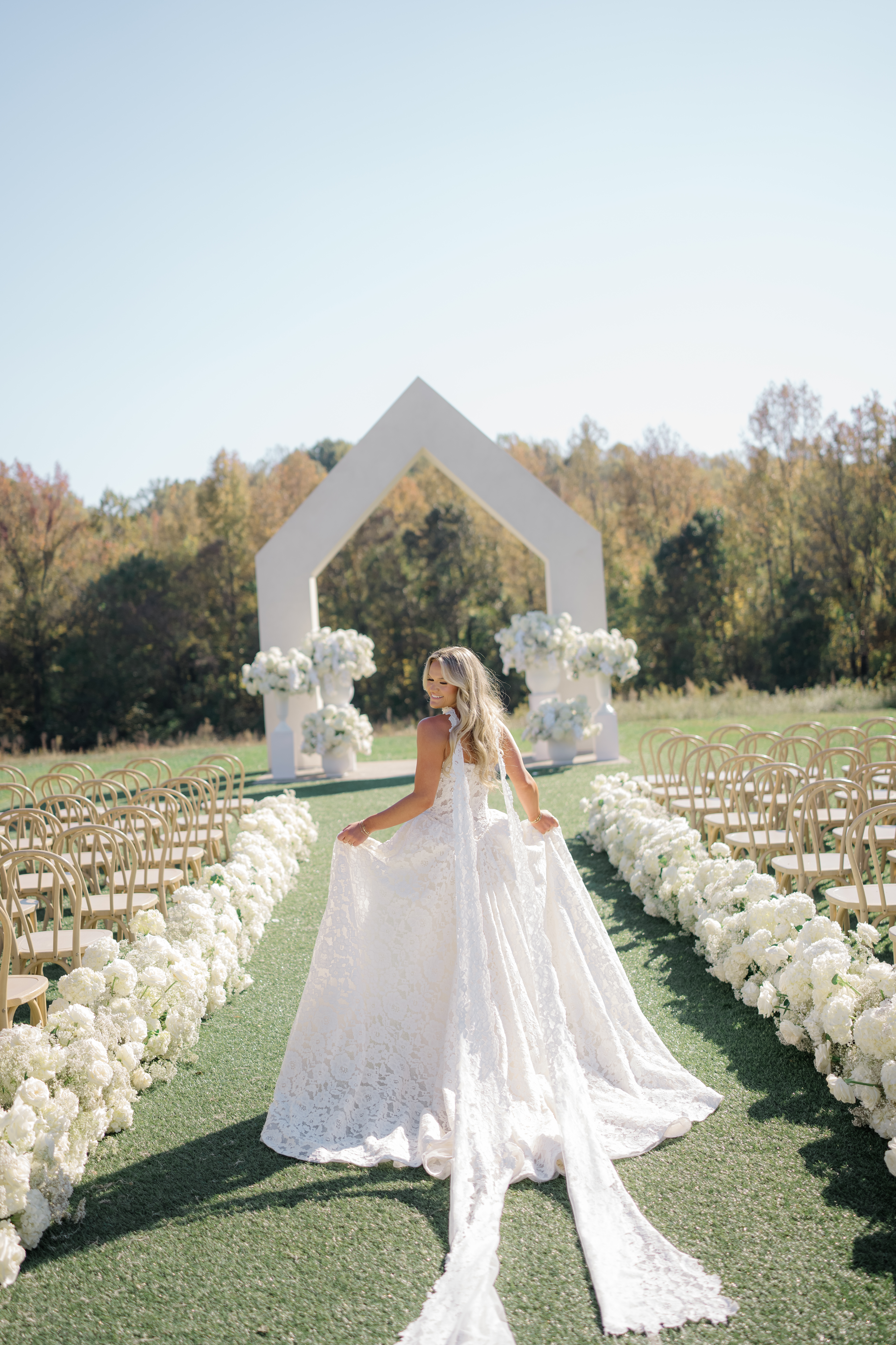 A bride posing in front of a modern wedding ceremony arch with a long train and flowing dress.
