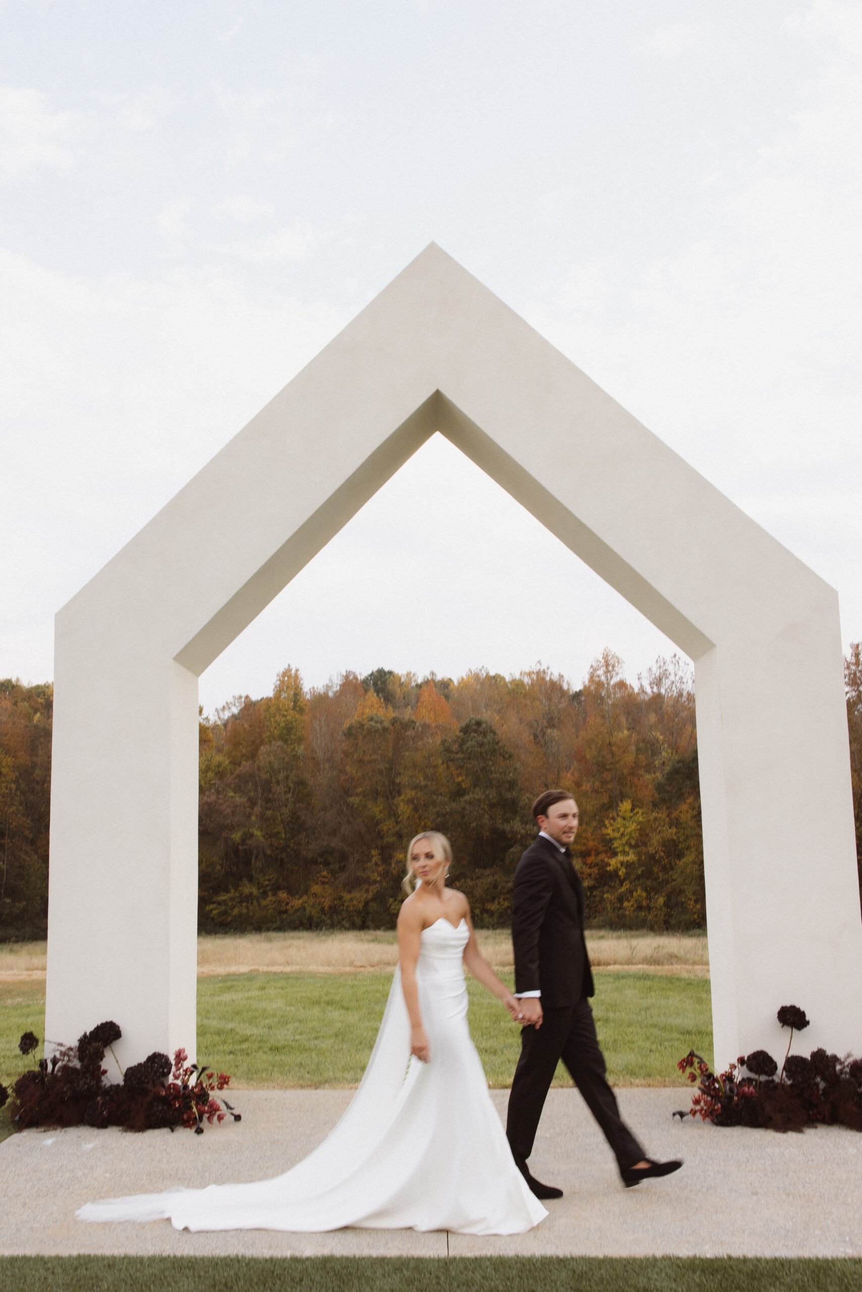 A bride and groom walking hand in hand beneath a modern ceremony arch.