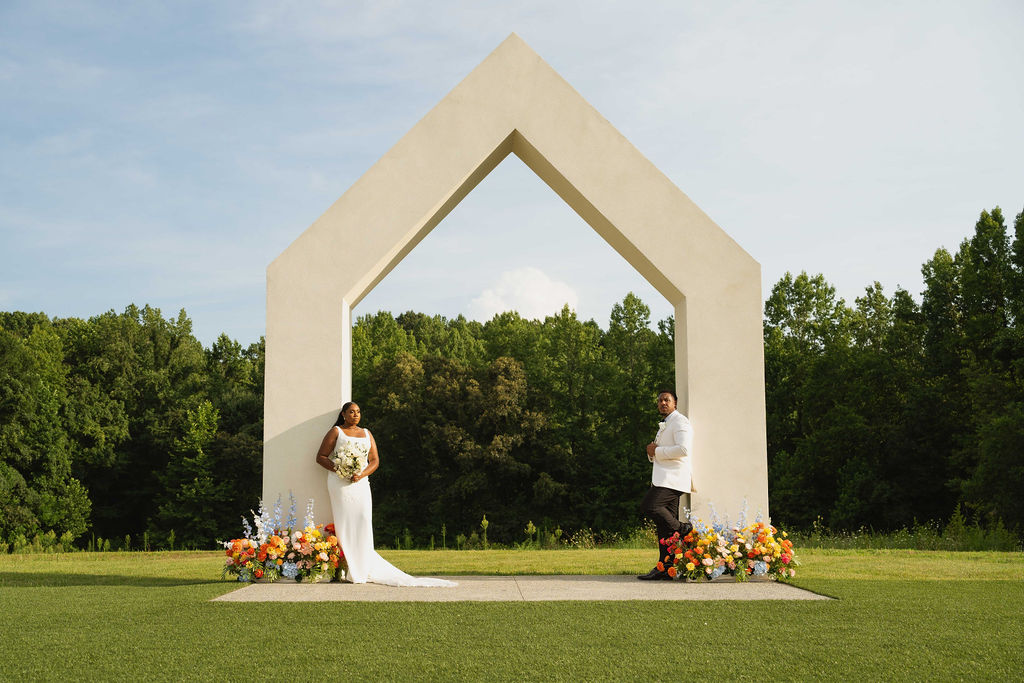 Bride and groom posing beneath a modern wedding ceremony arch.