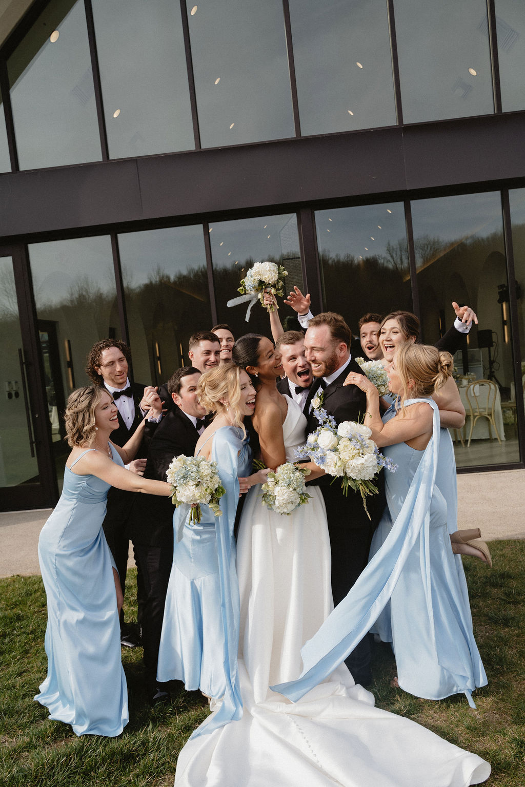 A bridal party cheers and throws their hands up, surrounding the newlyweds.
