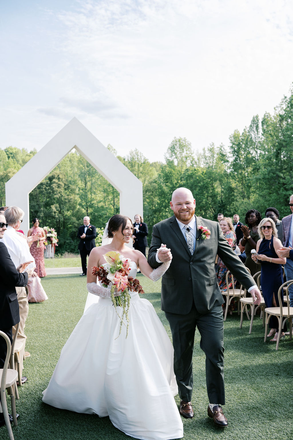 A bride and groom walk hand in hand back down the outdoor aisle after saying 'I do'.