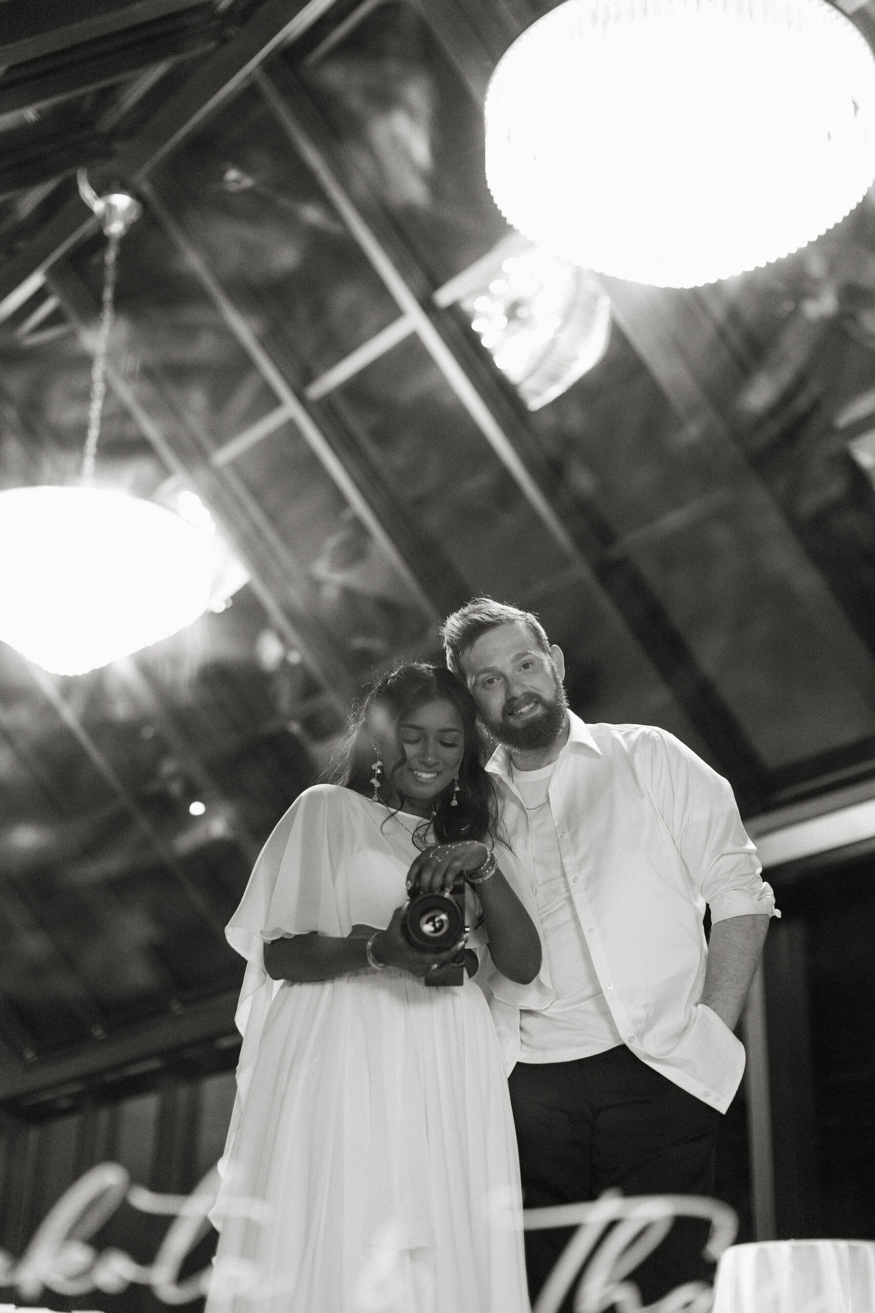 A bride and groom taking a mirror selfie with a camera at the end of their wedding day.