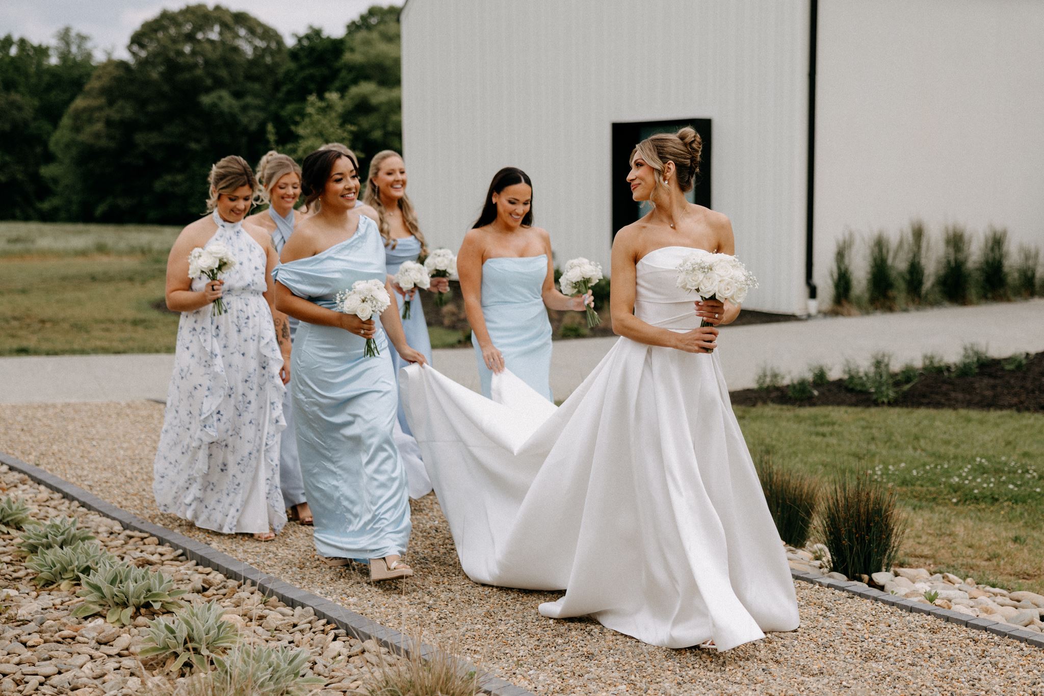 A bride and her bridesmaids dressed in blue dresses walking outside of their North Carolina venue.
