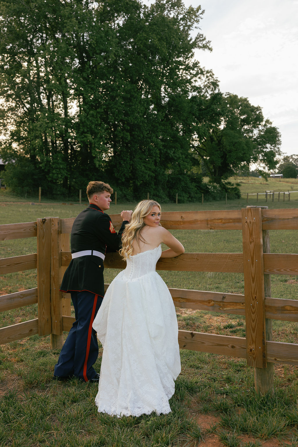 A bride and groom lean against a rustic wooden fence for portraits in North Carolina.