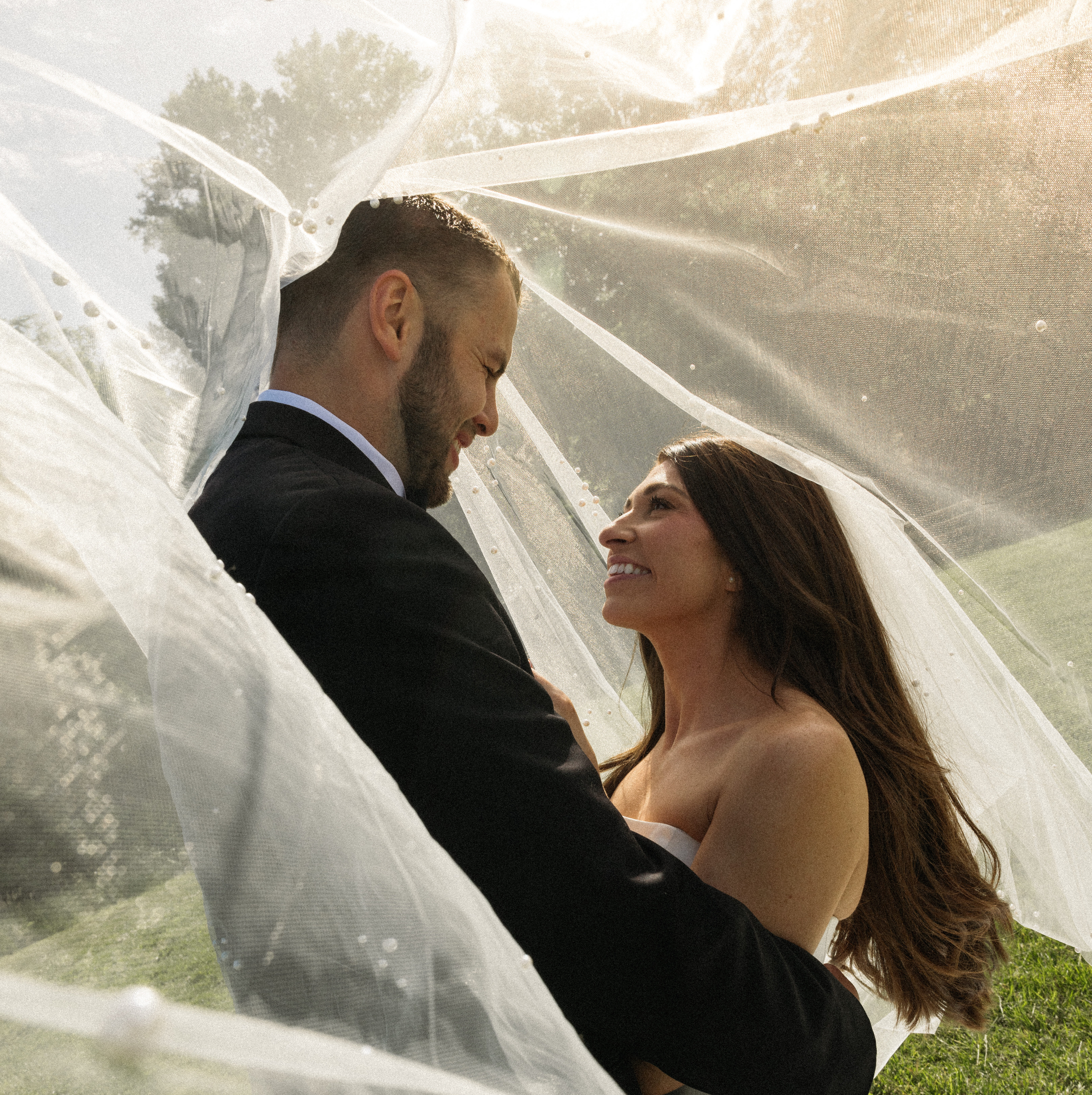 A bride and groom smiling beneath the bride's flowing veil.